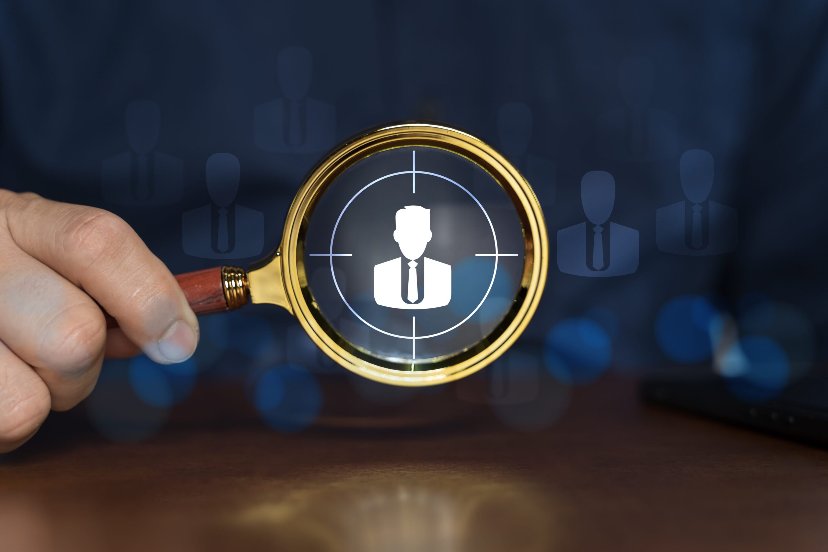 Magnifying glass focusing on a businessperson icon among others.